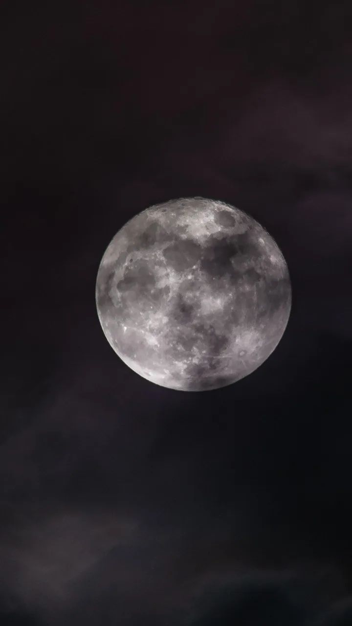 A full moon behind thin cloud in a dark sky